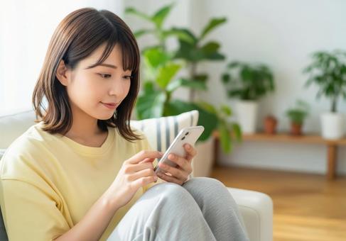 ソファーでスマートフォンを操作する女性 ソファーでスマートフォンを操作する女性の写真