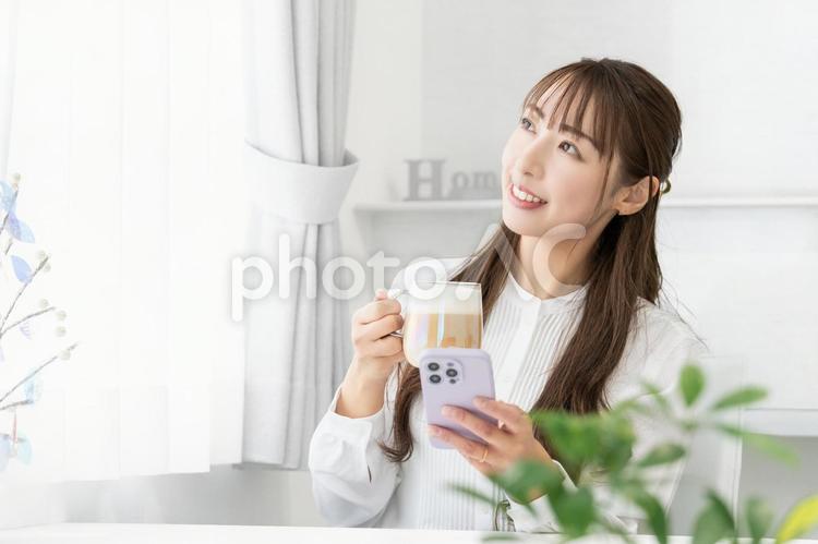 スマホを使いながら飲み物を飲む笑顔の女性 女性,人物,スマホの写真素材