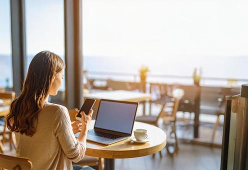 海見えるカフェで作業するフリーランス女性 海見えるカフェで作業するフリーランス女性の写真