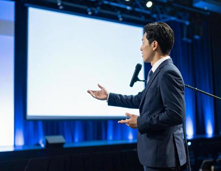 ステージ上で堂々とプレゼンする男性 ステージ上で堂々とプレゼンする男性の写真