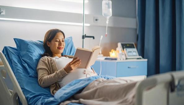 本を読んで安静にして点滴を打つ妊婦の写真