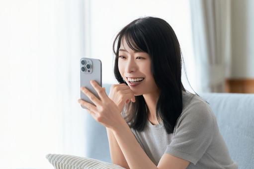 ソファに座ってスマホを使う笑顔の女性 女性,スマホ,スマートフォンの写真素材