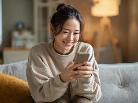 リビングでスマホを見る女性 リビングでスマホを見る女性の写真