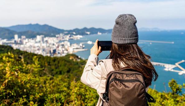 海の向こうを携帯で撮影する観光客の女性 海の向こうを携帯で撮影する観光客の女性の写真