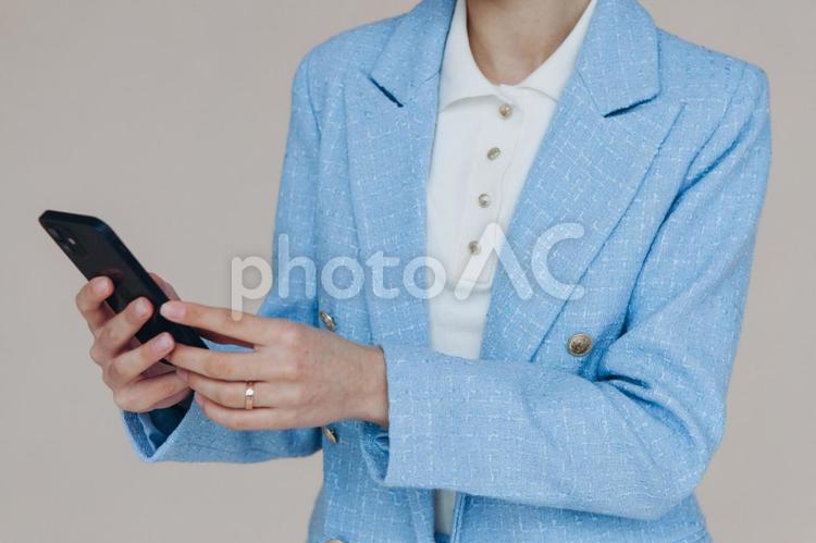 携帯を見ている女性の顔から下 手元,女性,水色の写真素材