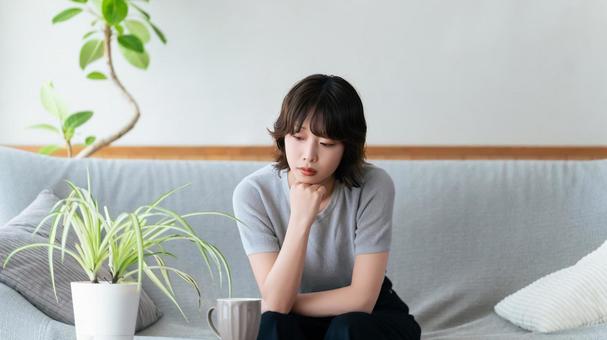 リビングのソファに座って考える女性 リビングのソファに座って考える女性 女性,考える,困るの写真素材