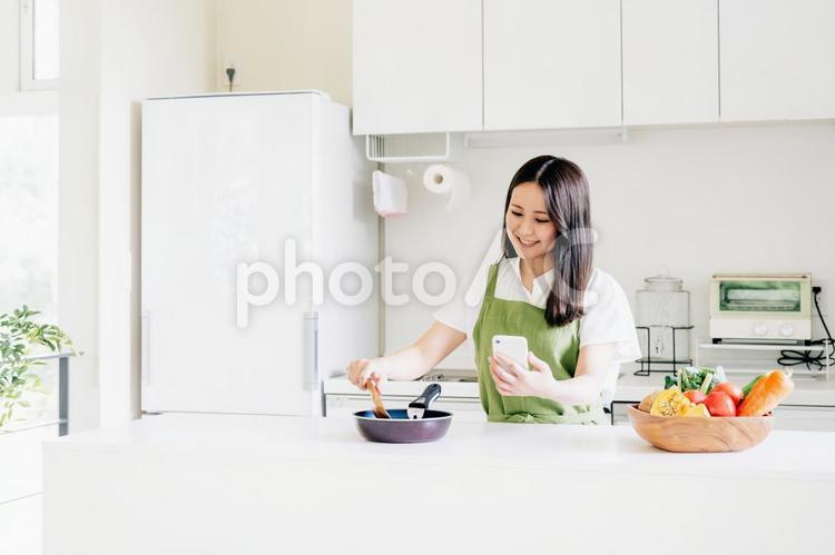 スマホを見ながら料理する女性（笑顔） 料理,家事,スマホの写真素材