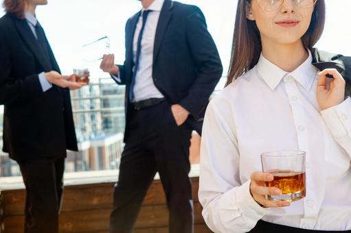 グラスを持ち微笑む女性と後ろの男性 ウイスキー,グラス,ウイスキーグラスの写真素材