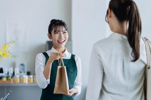 商品を渡す若い女性の店員 商品を渡す若い女性の店員の写真