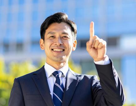 都市背景で人差し指を立てるビジネスマンの写真