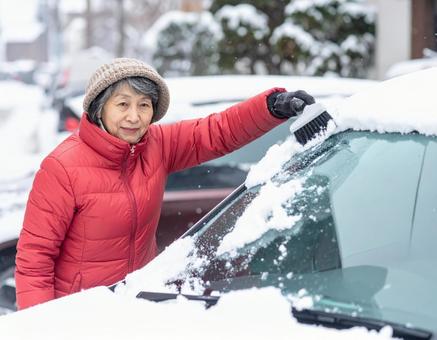 冬に車に積もった雪を雪下ろしする女性 冬に車に積もった雪を雪下ろしする女性の写真