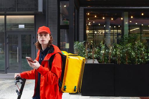 街なかでスマートフォンを使うフードデリバリーの男性の写真