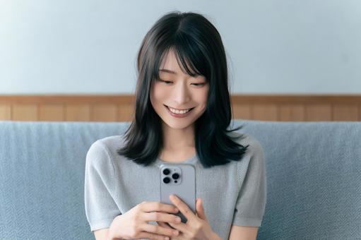 ソファに座ってスマホを使う笑顔の女性 ソファに座ってスマホを使う笑顔の女性の写真