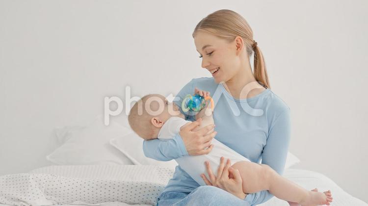 玩具を持つ赤ちゃんを抱っこ中の笑顔の女性 親子,抱っこ,見つめるの写真素材
