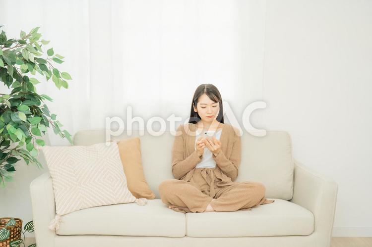 スマホを見てショックを受ける女性（ソファ） スマホ,悲しい,ショックの写真素材