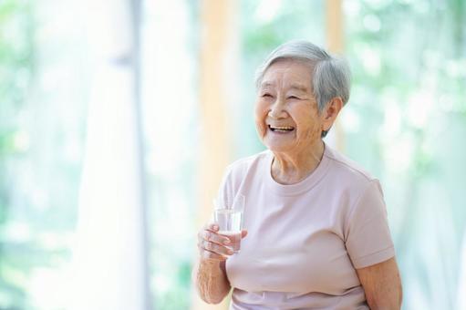 窓際でコップの入ったコップを持ち笑う女性 女性,コップ,水の写真素材