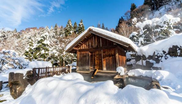 雪の積もる山中の湯気が立ち上る露天風呂の写真