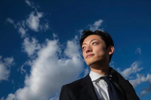 青空を見上げるビジネスマンの写真