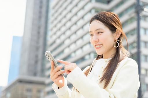 ビル街でスマホを操作する女性 ビル街でスマホを操作する女性 スマホ,元気,キャリアウーマンの写真素材