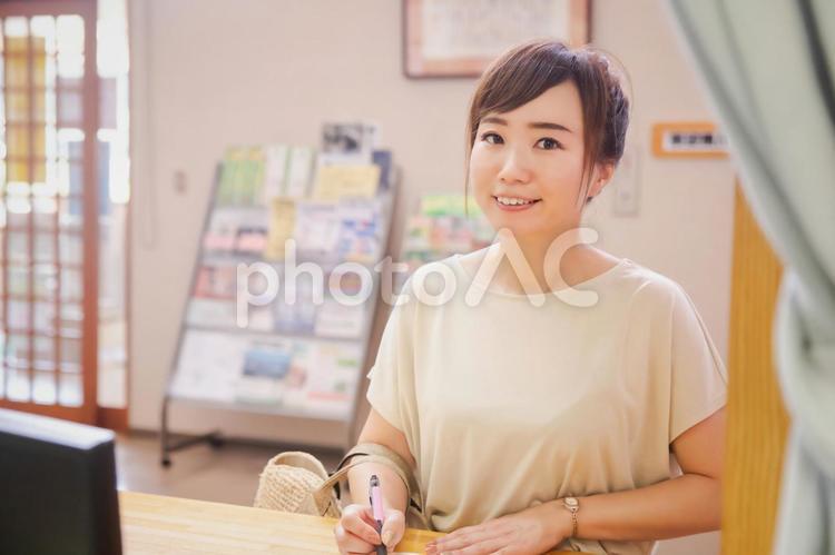 受付で何か書き込む女性 受付,チェックイン,カウンターの写真素材