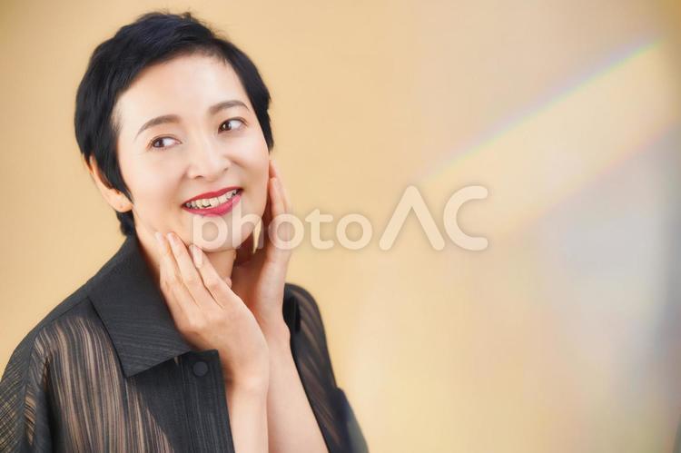 頬を触っているショートカットの女性（ベージュ背景） 女性,日本人,50代の写真素材
