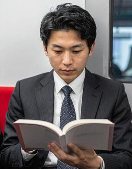 電車の中で本を読むビジネスマン男性 電車の中で本を読むビジネスマン男性の写真