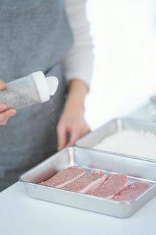 豚肉に塩胡椒で味付け中の手元 豚肉に塩胡椒で味付け中の手元の写真