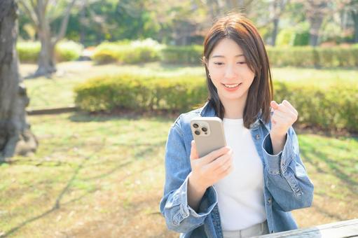 スマホを持ってガッツポーズをする女性 スマホを持ってガッツポーズをする女性の写真