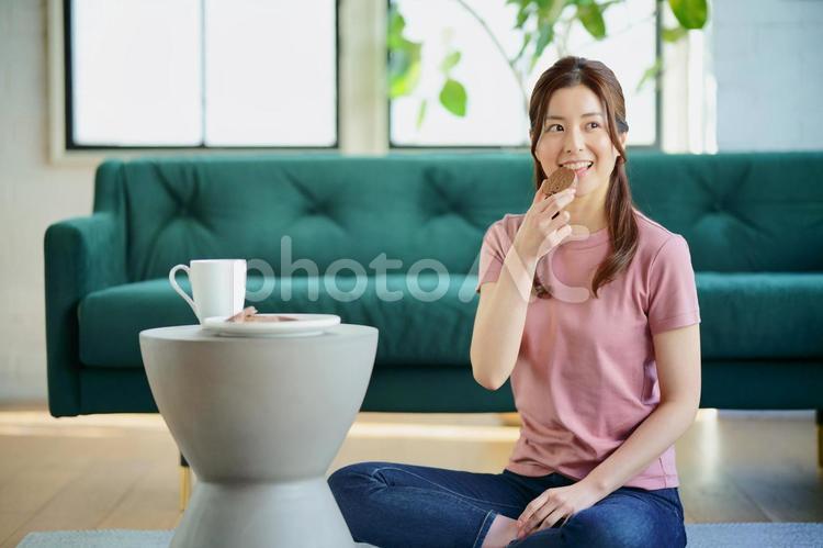 リビングの床に座って椅子をテーブルにしておやつを食べている女性 女性,日本人,1人の写真素材