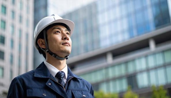 高層ビルの斜め上を見つめる若い作業服男性 高層ビルの斜め上を見つめる若い作業服男性の写真
