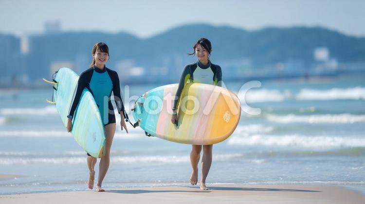 海辺の砂浜でサーフボードを抱え歩く女性 夏,海辺,サーフィンの写真素材