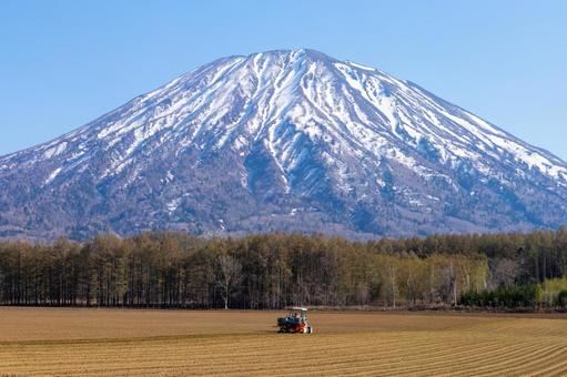 春の畑と雪の残る羊蹄山 春の畑と雪の残る羊蹄山 羊蹄山,トラクター,畑の写真素材