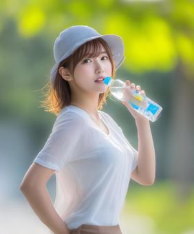 水分補給をする帽子を被った女性 水分補給をする帽子を被った女性の写真