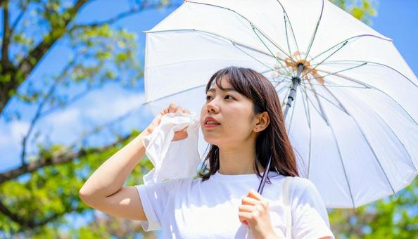 日傘をさして白いハンカチで汗を拭く女性 日傘をさして白いハンカチで汗を拭く女性の写真