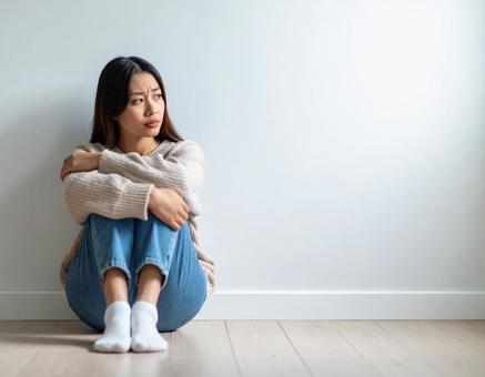 不安そうに部屋の隅で座り込む女性 不安そうに部屋の隅で座り込む女性の写真