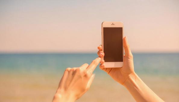スマートフォンで海を撮影する女性の手 スマートフォンで海を撮影する女性の手の写真