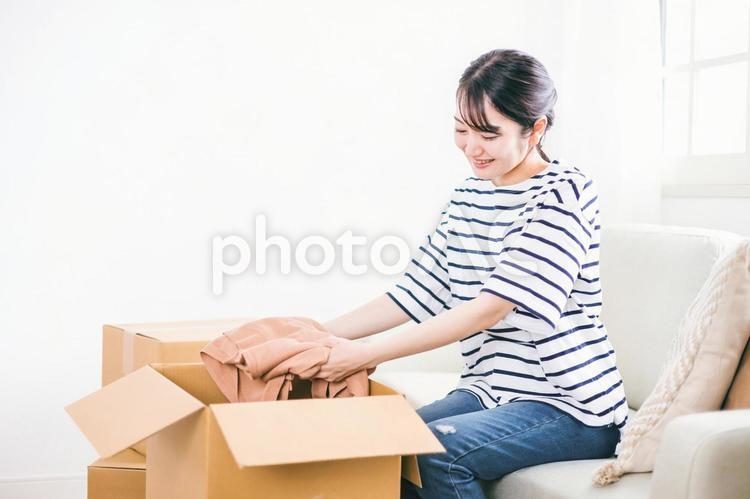 ダンボール箱から笑顔で洋服を取り出す女性 引越し,新生活,転居の写真素材