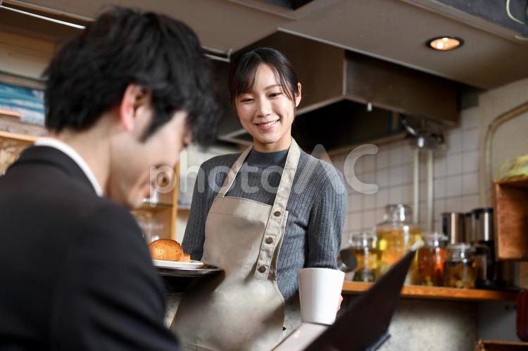 飲食店で男性客に食事の配膳をする女性店員 飲食店,レストラン,カフェの写真素材