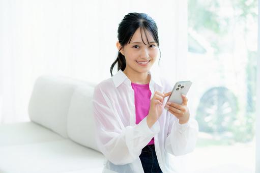 部屋でスマホを操作する若い女性 スマホ,若い女性,笑顔の写真素材