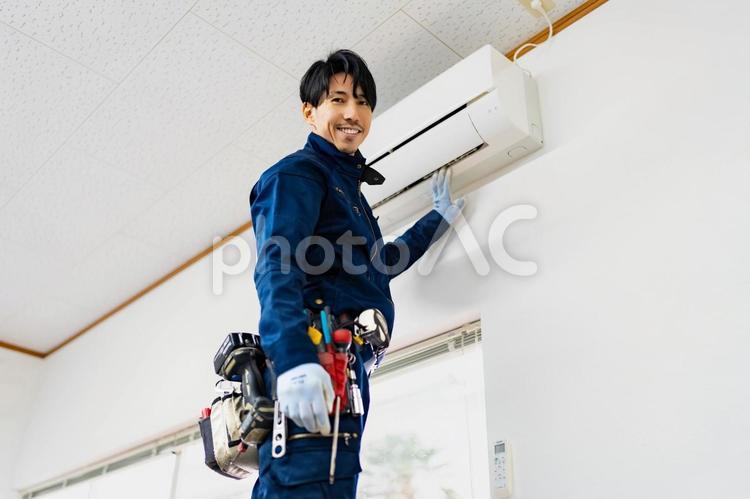 エアコン設置中に笑顔で立つ電気工事作業員 ビジネス,ビジネスマン,男の写真素材