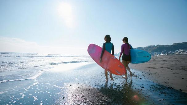海辺の砂浜でサーフボードを抱え歩く女性 海辺の砂浜でサーフボードを抱え歩く女性の写真