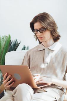 椅子で足を組んでノートパソコンを使う若い男性 男性,外国人,欧米人の写真素材