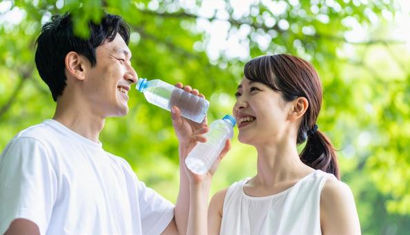 緑の中で水分補給する日本人男女 緑の中で水分補給する日本人男女の写真