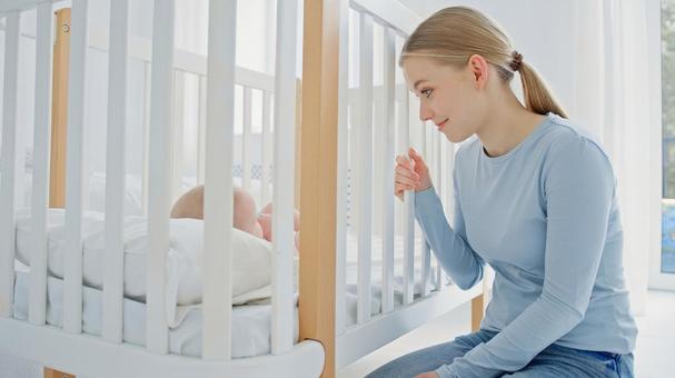 ベビーベッドの柵を握り赤ちゃんを見つめる笑顔女性 ベビーベッドの柵を握り赤ちゃんを見つめる笑顔女性 女性,ベビーベッド,見るの写真素材