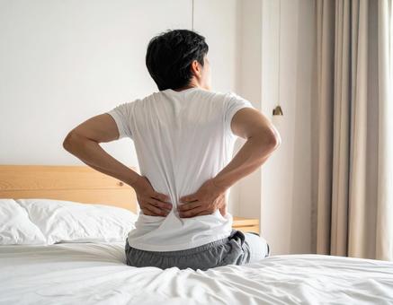 ベットの上で腰を抑えて苦しむ男性の写真