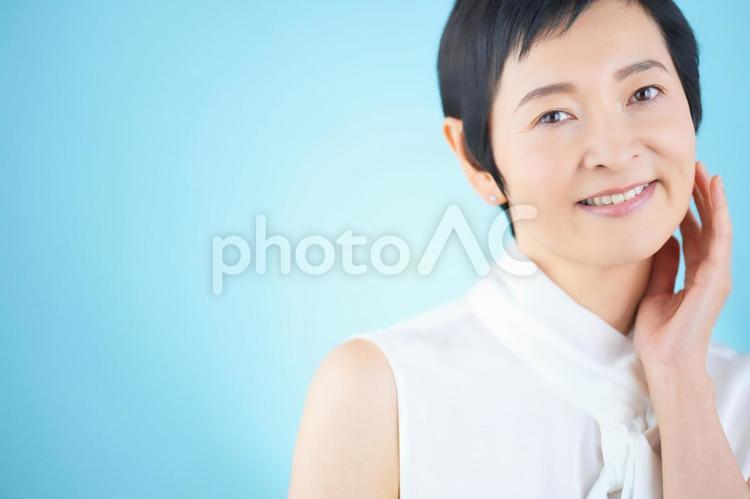 頬を触っているショートカットの女性（水色背景） 女性,日本人,50代の写真素材