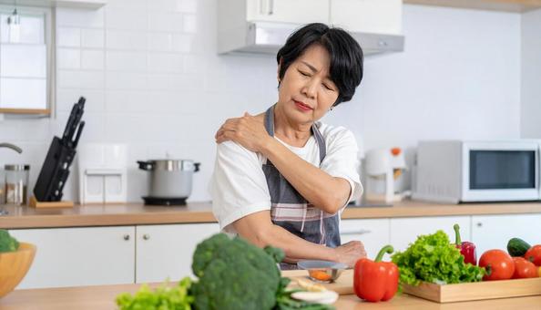 キッチンで肩こりを感じるエプロン姿の女性 キッチンで肩こりを感じるエプロン姿の女性の写真