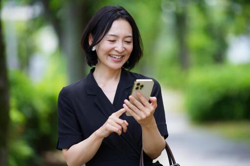 バッグを持ちスマホを見る笑顔の女性 女性,スマートフォン,操作の写真素材