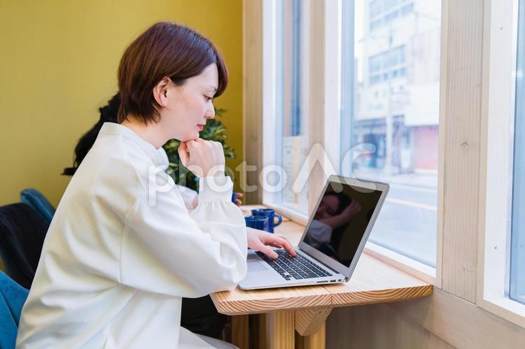 カフェの窓際カウンター席にいる女性（ノートパソコン） 考える,困る,難しいの写真素材