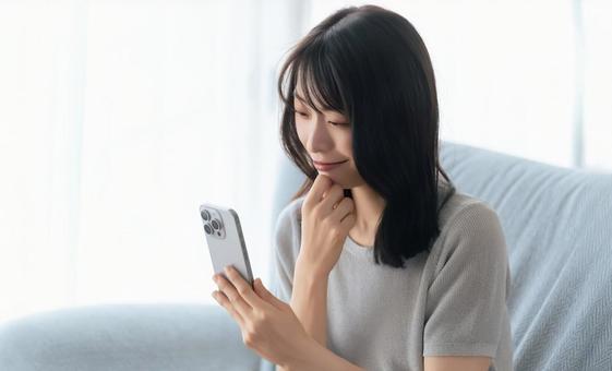 ソファに座ってスマホを使う笑顔の女性 ソファに座ってスマホを使う笑顔の女性 女性,スマホ,スマートフォンの写真素材